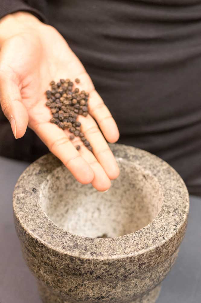 Hand hält Pfeffer über Mörser